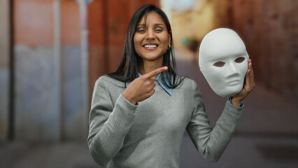 Woman smiling holding mask on street in outdoor urban setting with colorful backdrop, showcasing cheerful expression highlighting creativity and street art vibe. © Krakenimages.com