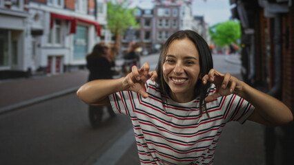 Woman showing hands in a claw gesture while laughing and leaning forward on a cobbled street with...
