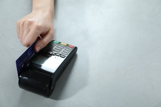 Woman with credit card using payment terminal at light grey table, closeup. Space for text