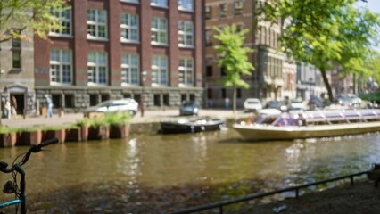 Blurred image capturing a defocused view of amsterdam canals with bokeh effect, featuring bikes and buildings under a clear blue sky in the netherlands.