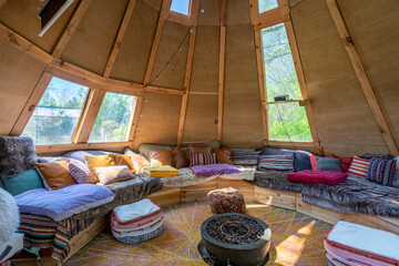 Cozy teepee interior with circular seating, wooden walls, colorful cushions and fire pit in eco glamping cabin © nagelsphoto