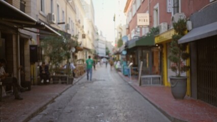 Obraz premium Narrow urban street scene blurred with soft bokeh and defocused storefronts along a cobblestone path, street; background backdrop copyspace calm.