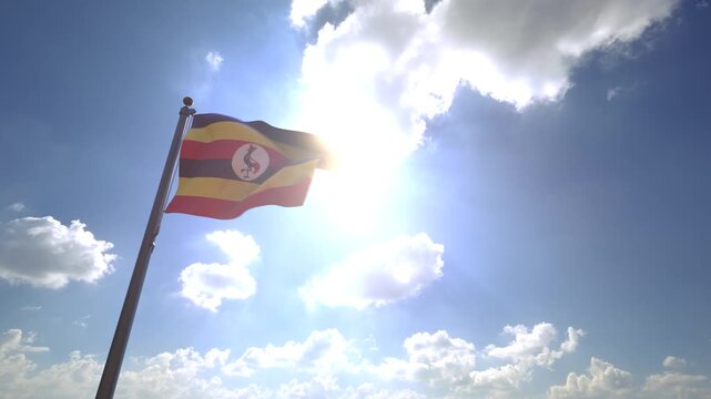 Uganda Flag waving on a Flagpole from a Moving Angle in front of a blue sky with clouds	