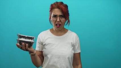 Woman holding stacked aluminum takeout containers with mouth open and raised hand in studio;...