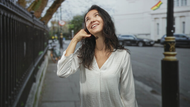 Woman in white blouse counting fingers on a city street while looking down at her hands and fingers and making small deliberate gestures; thoughtful reflection.