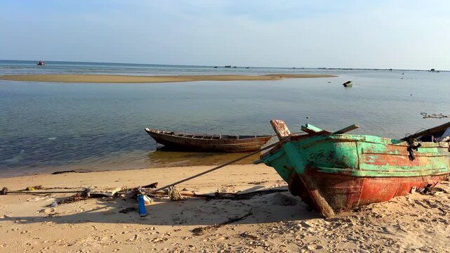 Abandoned boat on the ocean shore. An old, wrecked fishing boat on the beach by the sea near a fishing village on Phu Quoc Island in Vietnam.