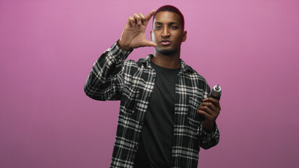 Obraz premium Young black man holding electric screwdriver and gripping trigger, pointing index finger toward camera while wearing plaid shirt in studio; confidence instruction.