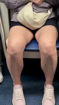 Knees And Sneakers On Subway Seated Commuter Legs Apart With Pink Canvas Shoes And Scuffed Soles, Casual Outfit, Crowded Carriage Ambience, Fluorescent Lighting, Everyday Urban Routine.