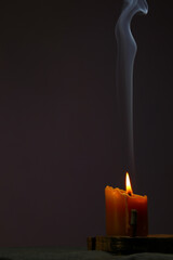 Naklejka premium Blue smooth texture smoke from incense aroma stick in motion rising above in holiday celebration and burning wax candle fire on copy space dark background. Yoga calm meditation, relaxation concept 