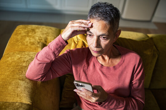 Concerned mature woman checking smartphone at home