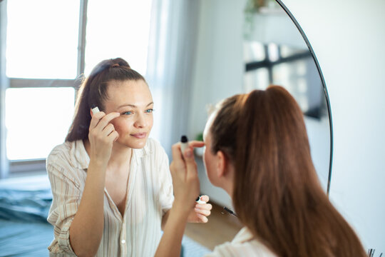 Young woman applying mascara at home mirror