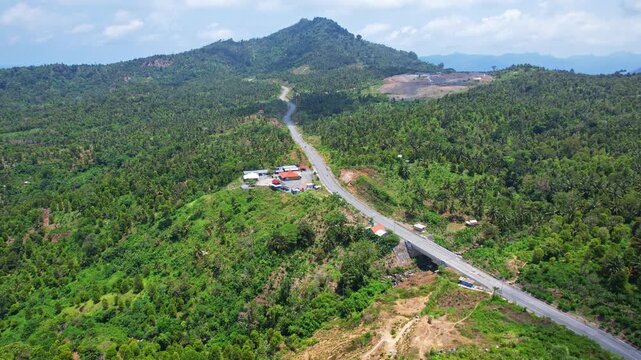 Aerial drone footage of a long part of Jalan Lintas Selatan, a new coastal road on the south coast of Java island, Trenggalek regency, Indonesia, with wide forests around and a hill