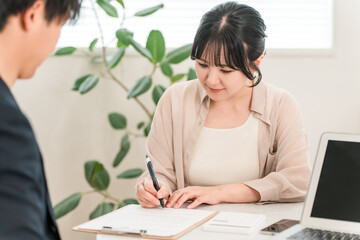 契約書,誓約書,同意書にサインする女性客と説明する男性ビジネスマン