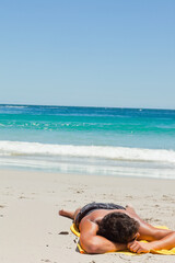 Naklejka premium Male is lying face down on yellow beach towel on pale sand with gentle waves breaking