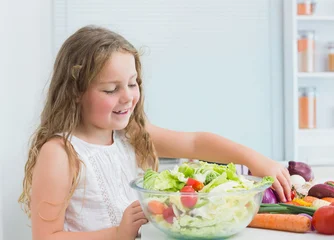 Fotobehang Koken Child female wearing sleeveless dress standing at kitchen counter preparing salad in glass bowl  © wavebreak3