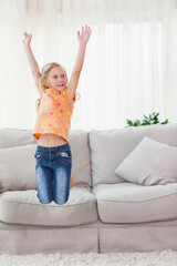 Child jumping on sofa in living room wearing orange polka-dot top and jeans with throw pillow