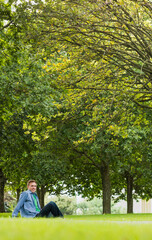 Large deciduous tree is spreading canopy over grassy lawn at park, with early yellowing leaves