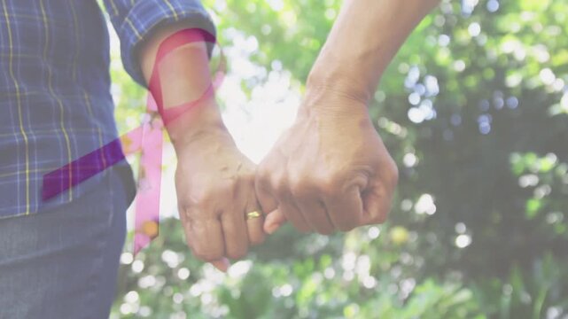 Senior couple linking pinkies after touch, tightening grip with pink ribbon overlay for health