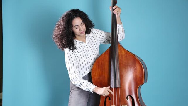 Woman playing double bass on light blue background