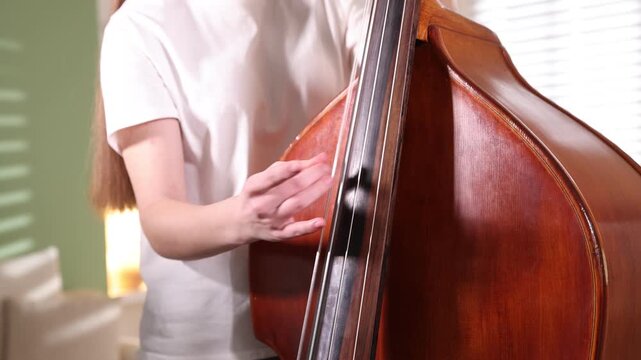 Teenage girl playing double bass at home, closeup