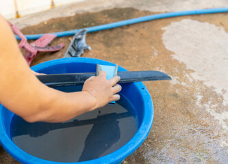 A person hand wet sanding a black plastic car part with blue sandpaper.