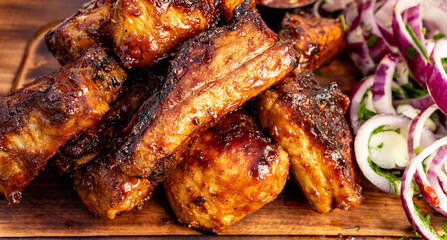 Grilled meat wings on a wooden platter with onions and green peppers nearby