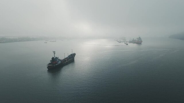 Aerial view of multiple oil tankers waiting in line at an oil refinery port in Cilacap, Indonesia, during heavy morning fog, illustrating global energy supply and maritime fuel logistics.