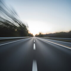 A long asphalt road stretches into the distance, trees blurred at the side, at sunset