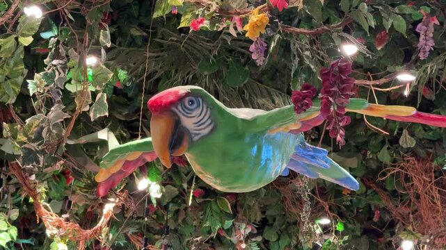 A colorful parrot statue spreads its wings among tropical leaves and flowers on the restaurant ceiling. Bright lights, green foliage and vivid feathers create a playful jungle atmosphere.