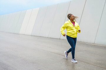 Obraz premium Active senior sport Afro Latina woman running outdoors in cool rainy weather – fitness, wellness and healthy lifestyle concept