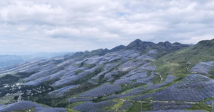 Aerial footage of large-scale solar photovoltaic farm on rocky desertification mountainous areas, renewable energy landscape under cloudy sky.  