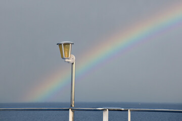 Naklejka premium A ship's lights against a backdrop of a rainbow before sunset at sea