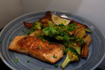 Horizontal photo of dinner with pan-seared salmon, roasted potatoes, and steamed broccoli on a blue plate&mdash;a healthy and visually appealing meal