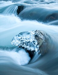 Frosted rock sits mid-stream, blurred water flowing over stones in hues of blue and white