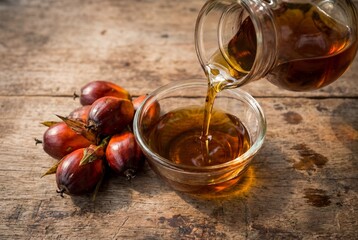Carafe pouring golden palm oil into bowl on rustic wooden table