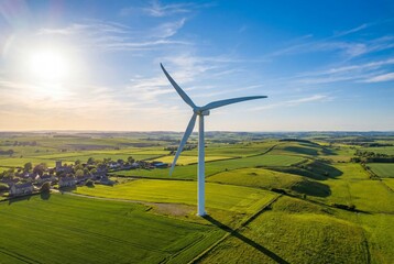 Obraz premium Large white wind turbine tower standing on green agricultural farmland under blue summer sky