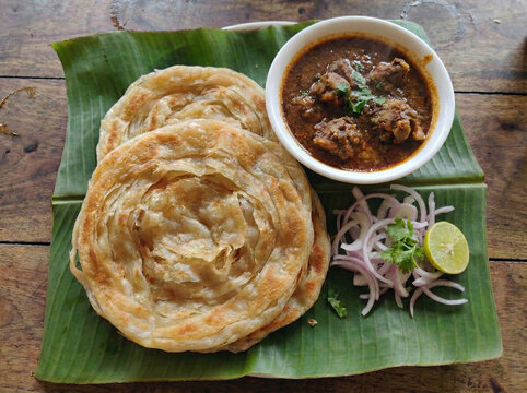 South Indian Madurai Parotta with Spicy Chicken Curry and Onion Salad Served on Banana Leaf Top View