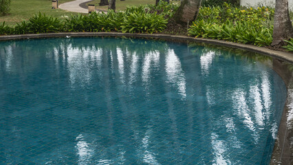 A fragment of an outdoor swimming pool. Clear water, blue tiled bottom. Green plants around the perimeter. A path winds through the lawn. Resort. Hotel. Mauritius.