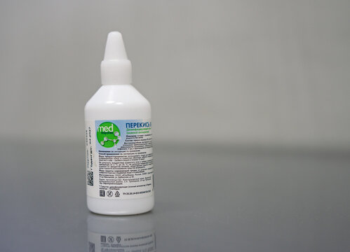  White bottle of 3% Hydrogen Peroxide solution on table on gray blurred background. White bottle of hydrogen peroxide on gray table background. Products for antiseptic. 