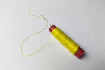 Needle stuck in the used yellow thread on a white background