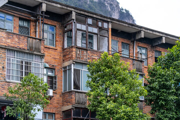 Fototapeta premium An aging brick apartment building with balconies and weathered facades in an older residential neighborhood in China. Urban housing, past-era construction, and poor living conditions