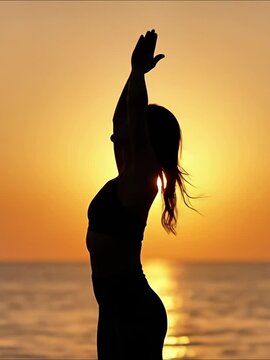 Woman doing yoga exercises near ocean at sunset, practicing meditation with arms outstretched, raised, and in prayer position