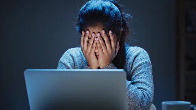 Concentrated young Indian woman working late on laptop in a dark room at night