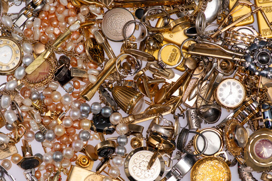 Antique jewelry lies in clutter on a gold background. The jewelry appears second hand. Gold metal defines the antique jewelry background. This background suggests pawnshop value.