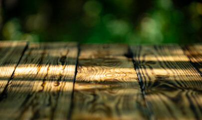 Wooden table top on blur green nature. Empty wooden desk top with green tree background. Wooden background with green nature. Wooden rustic texture near green blurred forest.