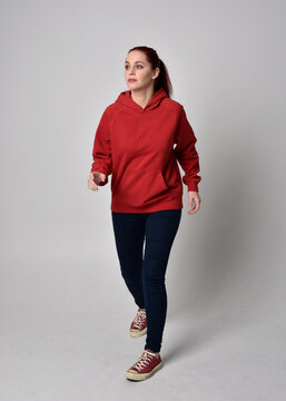 full length figure of female model wearing  basic contemporary casual clothing, red hoodie jumper, skinny jeans, sneakers. walking action pose, isolated white studio background.
