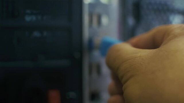 The hand inserts the blue flash drive into the slot on the back of the computer unit. The image is taken in close-up with an emphasis on action.