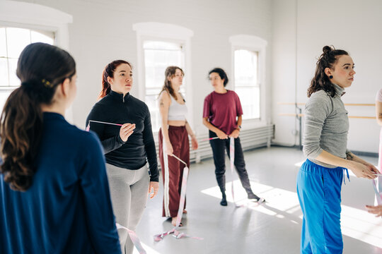 Dancers pause in studio holding ribbons during rehearsal
