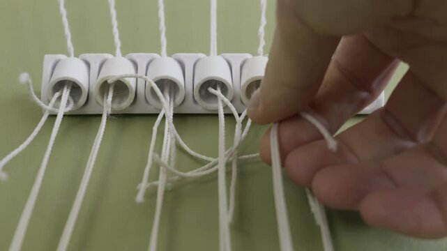 A hand pulls a white plastic cylinder threaded with string out of a holder on a green surface. Concept of home improvement, repair maintenance, and detailed manual assembly.