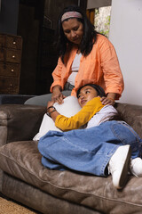 Mother holding belly and daughter resting across lap hugging stomach on sofa with white cushion